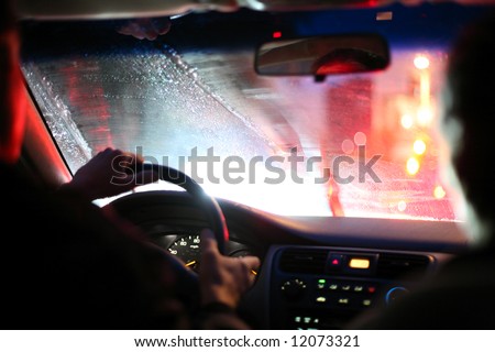 Driver and passenger driving on a rainy night in a city, view from inside. Shallow DOF.