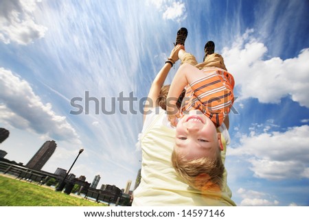 Happy young boy hanging upside down on mother\'s back over blue sky.