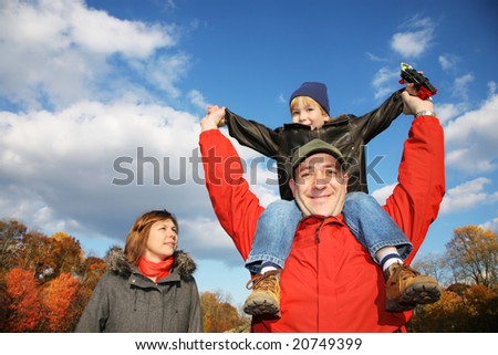 Young family in autumn park. Father holding his son on his shoulders against blue sky.