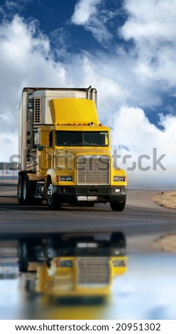 Big yellow trailer on the road over dramatic blue sky with white clouds.