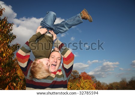 Happy father lifting son upside down over blue sky