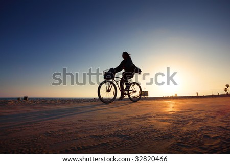 Biker silhouette riding along beach at sunset