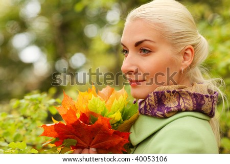 Portrait of beautiful young woman with bunch of autumn leaves in park.