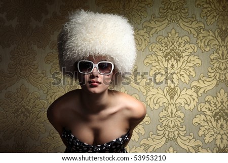 Portrait of beautiful sexy young woman in white fur hat posing over golden vintage floral wallpaper background.