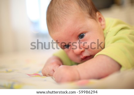 Newborn baby girl lying on bed, lifting the head up. Close-up, shallow DOF.