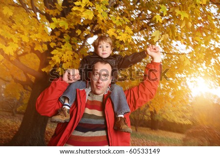 Portrait of happy father giving son piggyback ride on his shoulders in autumn park.