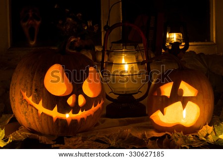 Photo composition from two pumpkins on Halloween. Jack and frightened pumpkins stand against dry leaves, candles and an old window in which the ghost looks