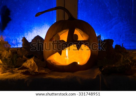 Pumpkin photo for a holiday Halloween. The scared pumpkin against an old window, candles and leaves with blue illumination