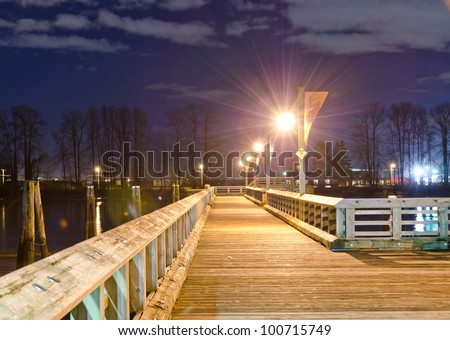 Fantastic view of the wooden pier, promenade, road, path in the park along the river ( ocean ) bank at night, dick time. Vancouver, Canada