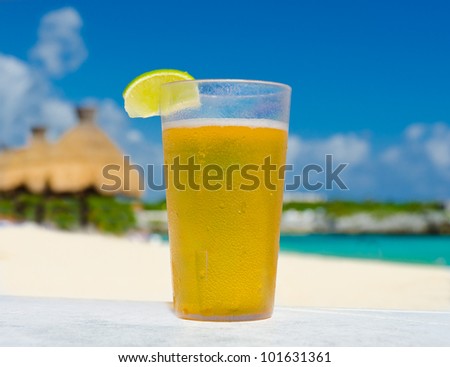 Glass with lemonade   ( beer, ice tea ) on the tropical beach with a resort as a background.