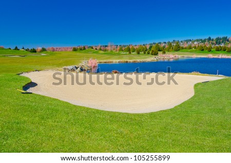 Sand bunker on the golf course with the pond and dark blue sky.