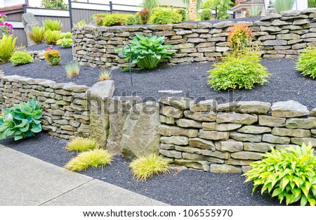Some flowers and nicely trimmed bushes on the leveled with stones front yard. Landscape design.