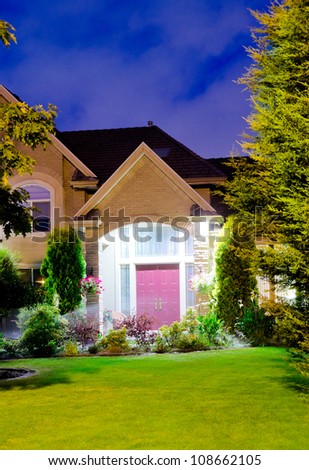 Fragment of a big luxury house with the triple garage doors at dusk, night time.