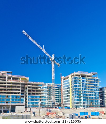 High-rise building under construction. The site with cranes against blue sky. Vancouver, Canada.