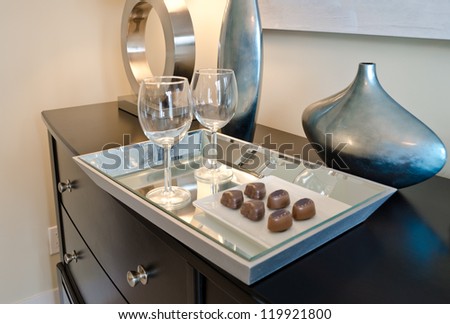 A tray  the  with wine glasses  and some chocolate candies  on top of the dresser. Interior design.