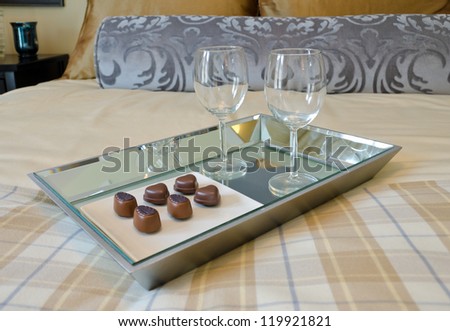A tray on the bed with wine glasses and some chocolate candy