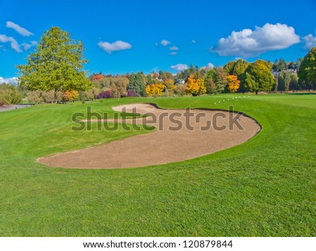 Golf course with gorgeous green and sand bunker and dark blue sky with white clouds as a background.