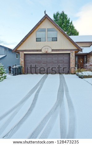 Double doors garage winter time with tire tracks on the long driveway