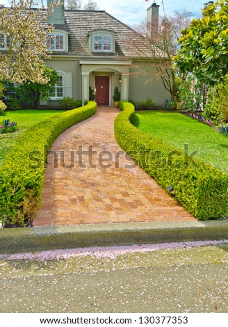Stoned, paved house doorway, trail with nicely trimmed and landscaped bushes in front of the house entrance.