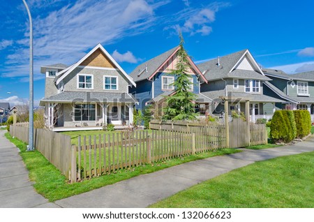 Comfortable neighborhood. Some middle class homes with nicely landscaped front yard lawn behind the wooden fence in the suburbs of the North America. Canada.
