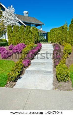 Some flowers and nicely trimmed bushes aside the doorway steps. Landscape design.