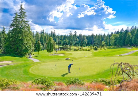 Beautiful golf course with a playing golfer in a sunny day with dark blue sky and clouds. Canada, Vancouver.