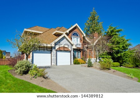 Big custom made luxury house with two doors garage, long driveway and  nicely trimmed and landscaped front yard lawn in the suburbs of Vancouver, Canada.