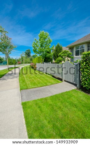 Nice and clean sidewalk at the empty street and wooden fence aside. Neighborhood scenery, landscape design.