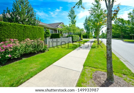 Nice and clean sidewalk at the empty street and trimmed green and wooden fence aside. Neighborhood scenery, landscape design.