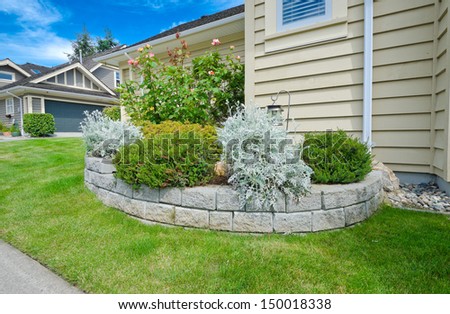 Some flowers and nicely trimmed bushes on the leveled front yard flowerbed. Landscape design.