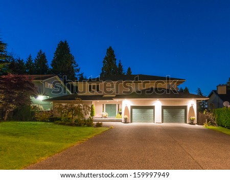 Big luxury house with two garages and long nicely paved driveway at dusk, night time in suburbs of Vancouver, Canada.