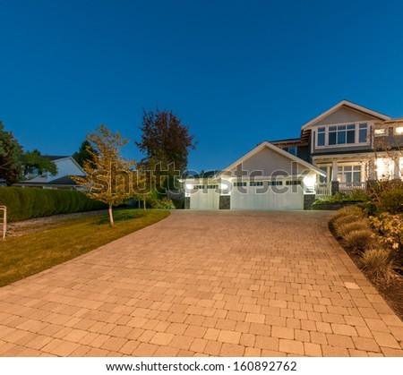 Wide and long driveway to double doors garage of a big luxury house at night, dusk time in suburbs of Vancouver, Canada.