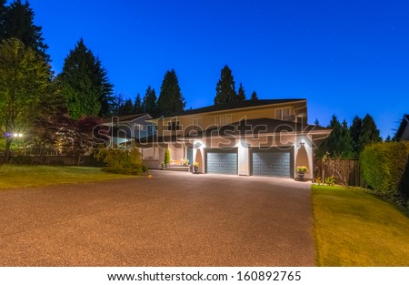 Big luxury house with two double doors garages and wide driveway at night, dusk time in suburbs of Vancouver, Canada.