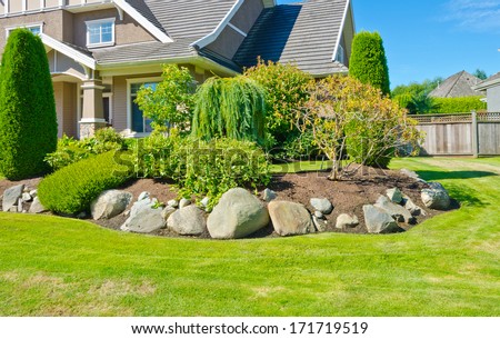 Flowers, stones and nicely trimmed bushes in front of the house, front yard. Landscape design.