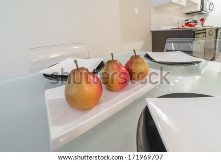 Nicely decorated dinner table with some plates and Fruit-piece, tray with three pears on the plate and the modern kitchen at the back. Interior design.