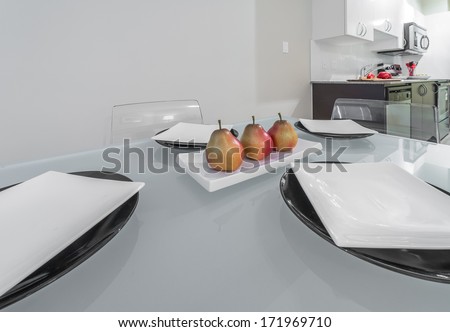 Nicely decorated dinner table with some plates and Fruit-piece, tray with three pears on the plate and the modern kitchen at the back. Interior design.