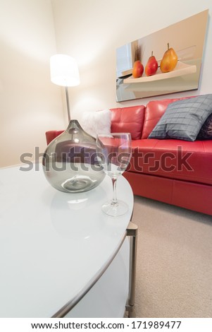 Fragment of luxury living suite. Nicely decorated modern family, living room with decorative vase and vine glass on the coffee table and red color leather couch. Interior design. Vertical.