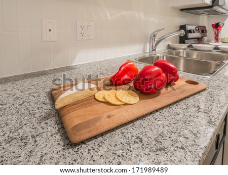 Wooden cutting board on the kitchen counter with some cheese and red pepper. Interior design.
