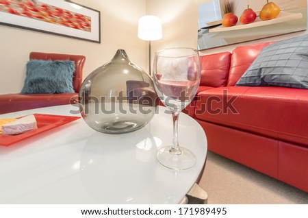 Fragment of luxury living suite. Nicely decorated modern family, living room with decorative vase and vine glass on the coffee table and red color leather couch. Interior design.