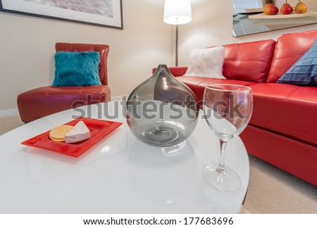 Fragment of luxury brand new living suite. Nicely decorated modern family, living room with decorative vase and vine glass on the coffee table and red color leather couch and chair. Interior design
