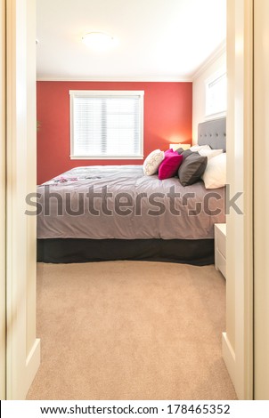View through the open doors at the modern comfortable and elegant luxury master bedroom with red color wall. Interior design. Vertical.