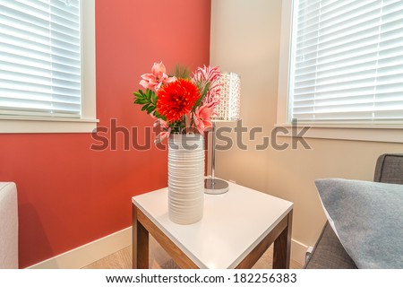 Fragment of a luxury living suite. Nicely decorated modern family, living room with decorative vase with some flowers on the coffee table and red colored room. Interior design.