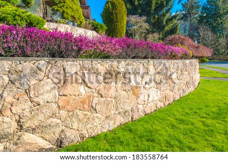 Leveled and stoned curved front yard with some flowers and nicely trimmed bushes and grass. Landscape design.