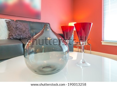Fragment of luxury suite. Nicely decorated modern family, living room with red color wall  and decorative vase and two vine glasses on the coffee table and leather couch at he back. Interior design.