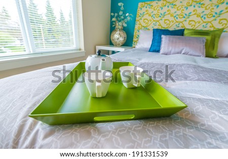 Decorative green color tray with the tea, coffee set on the bed in the luxury master bedroom. Interior design. Vertical.
