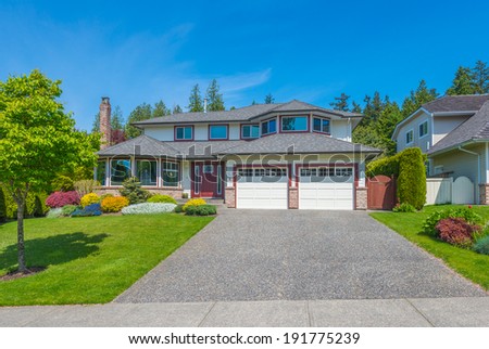 Custom built luxury house with nicely trimmed front yard, lawn and wide driveway to the double doors garage in a residential neighborhood. Vancouver, Canada.