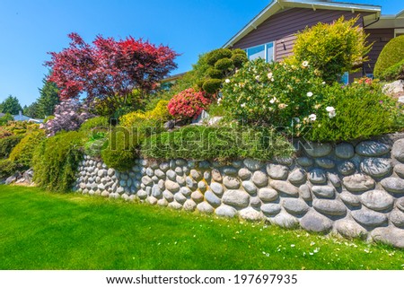 Some flowers and nicely trimmed bushes on the leveled and stoned front yard. Landscape design.