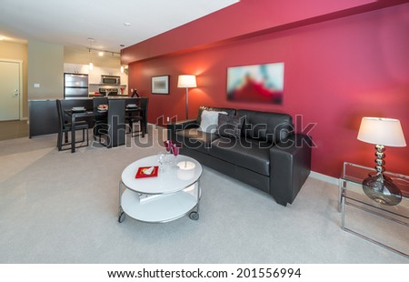 Perspective, outlook at the luxury living suite of brand new house: nicely decorated  living room with red walls, leather couch, coffee and dining tables and the kitchen at the back. Interior design.