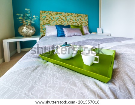 Decorative green color tray with the tea, coffee set on the bed in the luxury master bedroom. Interior design.