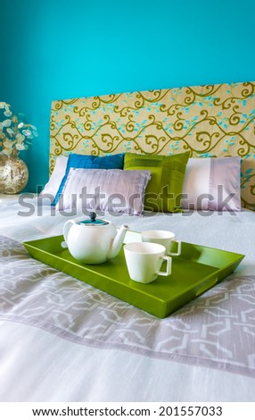 Decorative green color tray with the tea, coffee set on the bed in the luxury master bedroom. Interior design. Vertical.